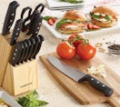 a block with knives on a counter with food on a cutting board