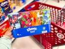 hand holding a 4-pack of kleenex tissues in front of target cart