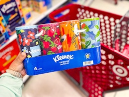 hand holding a 4-pack of kleenex tissues in front of target cart