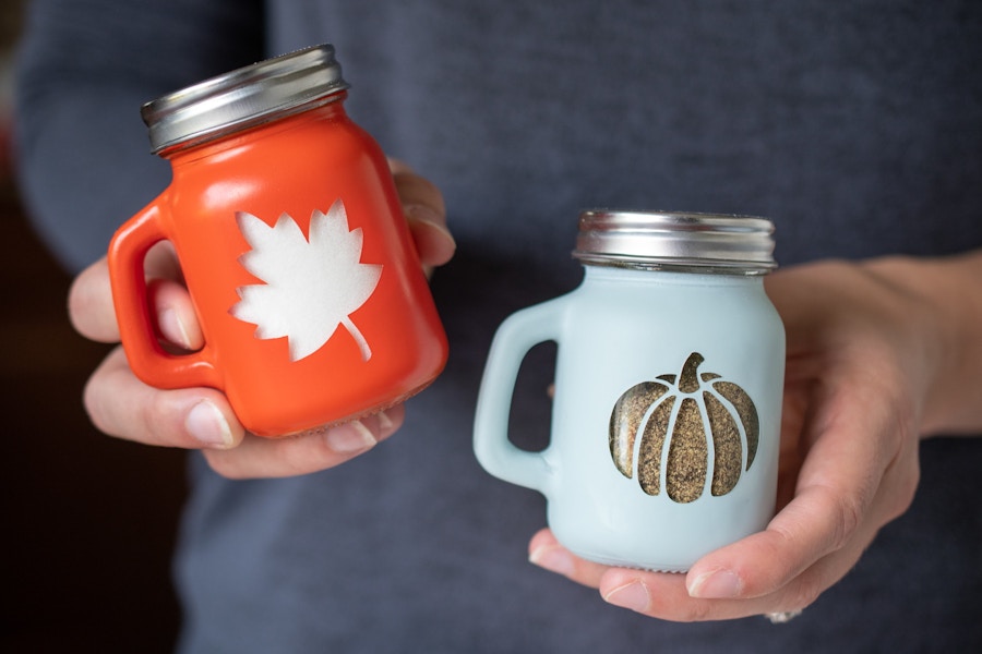 A person holding salt and petter shakes with a leaf and pumpkin on them.