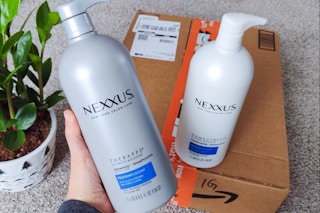 a person holding a nexxus shampoo bottle with an amazon box in the background