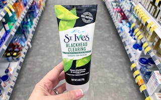 A hand holding St. Ives green tea face scrub in a store aisle