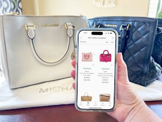 Someone looking at the Preowned Handbags on the Saks Off 5th app in front of some designer handbags on a table
