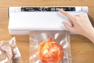 a hand touching a button on a vacuum sealer machine
