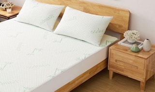 a bed in a room with a mattress cover and two pillows next to a wooden nightstand
