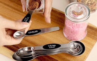 hands scooping seasonings out of a jar with stainless steal measuring spoons