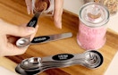hands scooping seasonings out of a jar with stainless steal measuring spoons