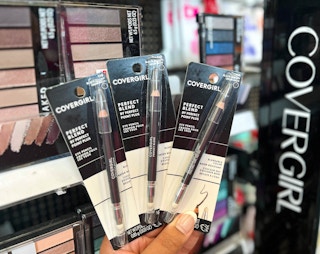 hand holding three packs of Covergirl eye pencils in front of display