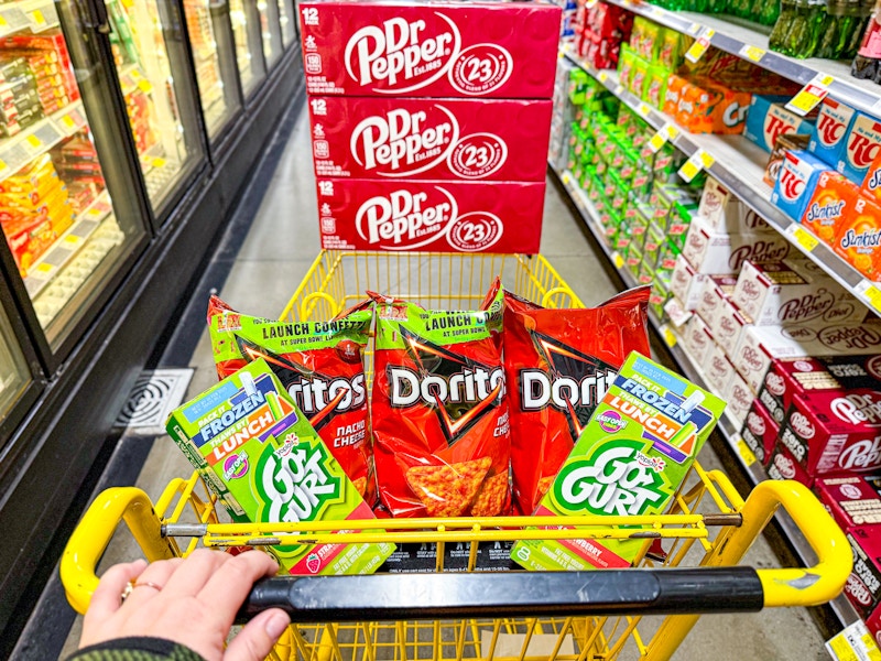 person pushing a cart with dr pepper, doritos, and gogurt in it