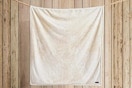 Beige Eddie Bauer Throw Blanket hung up on rope in front of wood panels