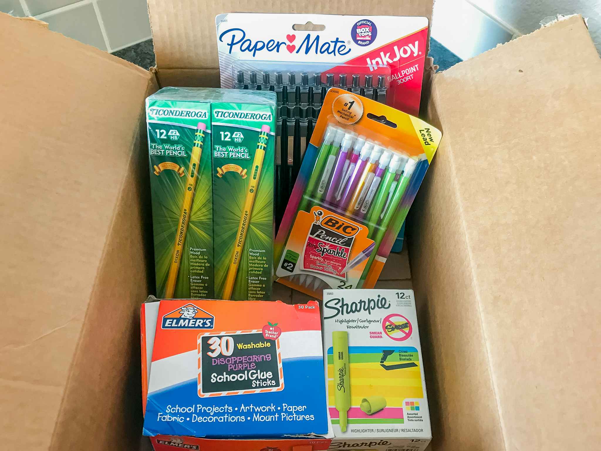 A box filled with school supplies including pencils, mechanical pencils, and glue sticks.