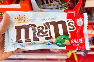 hand holding bag of m&ms candy in front of candy product shelves