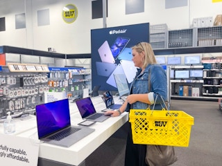 A woman looking at Apple laptops inside Best Buy.