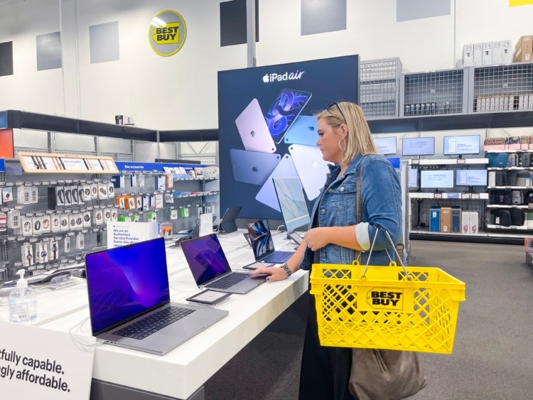 A woman looking at Apple laptops inside Best Buy.