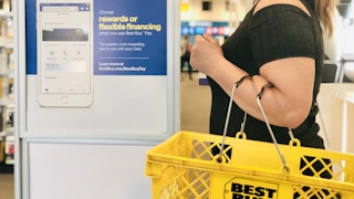 woman stands in front of a best buy rewards sign holding a yellow best buy shopping basket