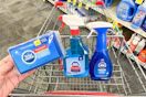 person holding sponges over a cart with window cleaner and dish spray in it