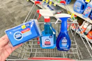 person holding sponges over a cart with window cleaner and dish spray in it