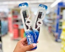 hand holding two Oral-B charcoal manual toothbrushes in aisle
