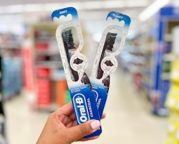 hand holding two Oral-B charcoal manual toothbrushes in aisle