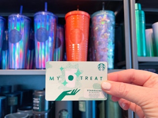 hand holding starbucks gift card near reusable cups