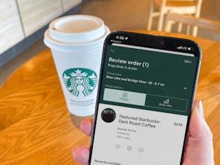 a person holding a cellphone with starbucks on screen in front of starbucks coffee