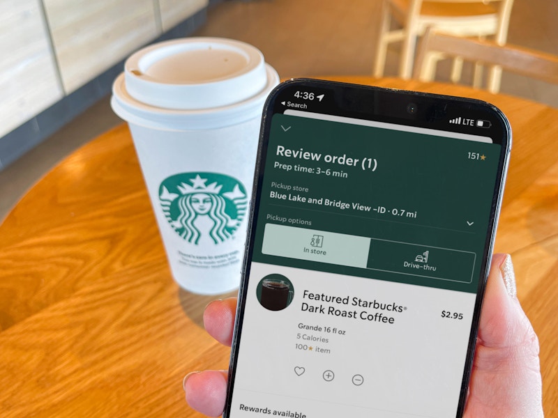 a person holding a cellphone with starbucks on screen in front of starbucks coffee