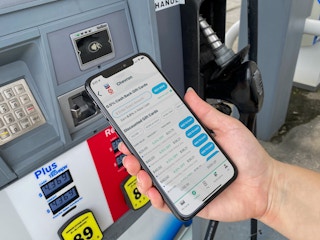 A person holding their phone displaying the Raise discount gift card app in front of a gas pump.
