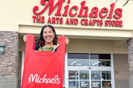 Woman holding out a shopping bag outside of a Michaels store