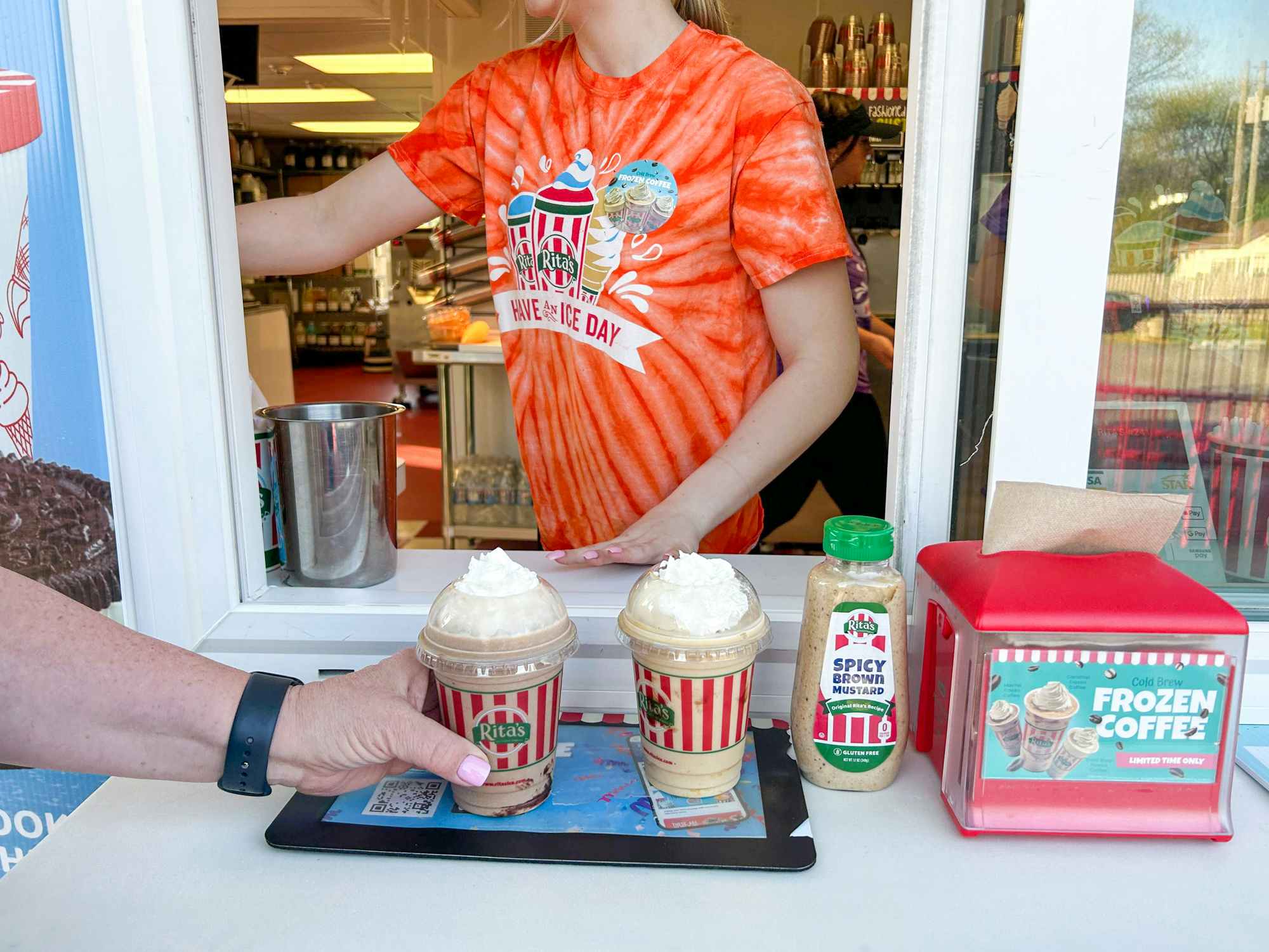 A Rita's employee serving some frozen coffees to customers