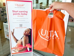 Someone holding an Ulta bag next to a sign for Ultamate Rewards inside an Ulta store