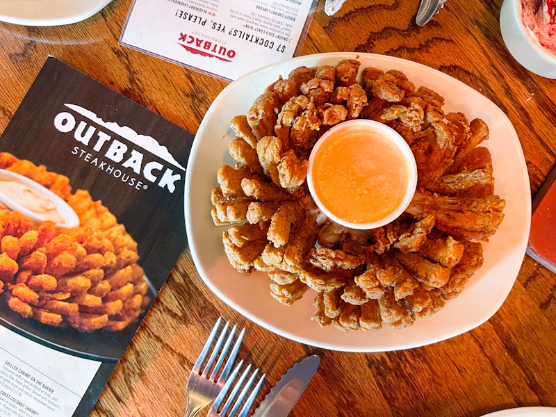 A Blooming Onion served on a table next to an Outback Steakhouse menu