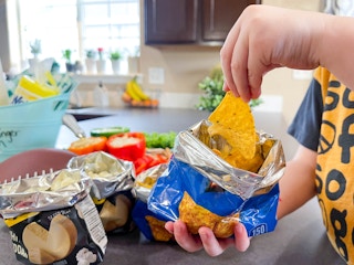 a child's hand grabbing a a chip from a bag of chips 