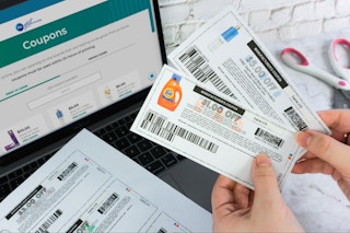 Someone holding some Procter & Gamble product manufacturer coupons in front of a laptop displaying the P&G website where they are ...
