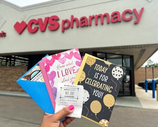 hand holding three Hallmark Cards with $3 ExtraBucks rewards in front of CVS storefront