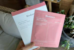 a hand holding a sheet mask in pink and white packaging