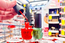 person holding the brush of a red opi nail polish bottle next to a bottle of green nail polish