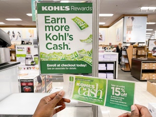 A person holding Kohl's cash near a Kohl's cash sign