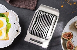 a silver egg slicer near plates of foods