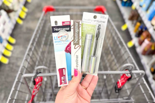 person holding neutrogena eyeliner, mascara, and lip oil over a cart