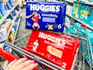 person pushing a cart with 2 packs of huggies diapers in it
