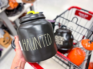 hand holding up a black rae dunn jar that says "haunted"