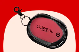 Black oval keychain pouch with pink center showing L'Oréal Paris logo and Target bullseye, on a red and cream background.
