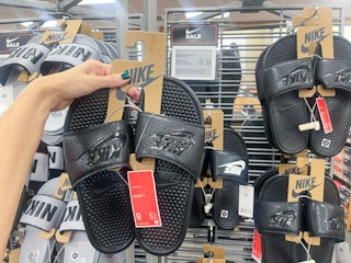 A pair of Nike slides held out in front of a store rack with other Nike slides.