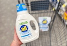 hand holding bottle of liquid detergent over shopping cart