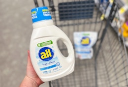 hand holding bottle of liquid detergent over shopping cart
