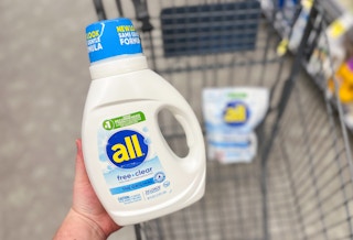 hand holding bottle of liquid detergent over shopping cart
