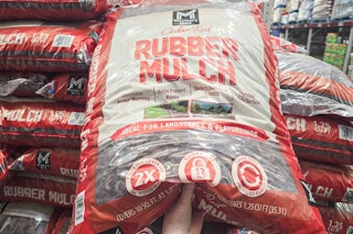 person grabbing a large bag of red rubber mulch