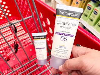 hand holding Neutrogena sunscreen in front of like item in Target cart