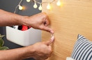 someone sticking a small clear hook on a wooden board