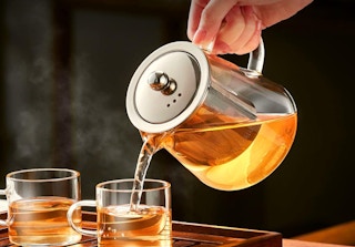 a person pouring tea into a mug from a glass teapot